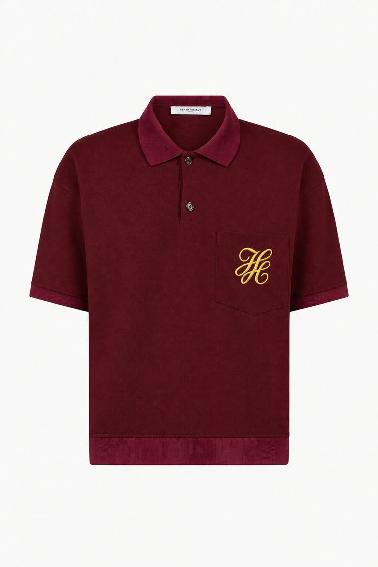IH NOM UH NIT FW26 burgundy short-sleeve polo shirt with yellow embroidered monogram on chest pocket, front view.